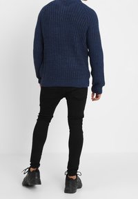 Granatowy sweter dzianinowy z teksturowanym wzorem, luźny krój, ściągacze przy mankietach i dole, zestawiony z czarnymi dopasowanymi dżinsami i czarnymi trampkami.