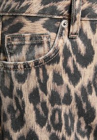 Leopardprint denim stof met tinten beige en zwart, voorzien van een opvallende textuur en gestikte details bij de zak.