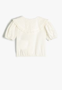 Weiße Bluse mit kurzen Ärmeln, die einen strukturierten, rüschenden Kragen, puffige Ärmel und einen elastischen Saum aufweist. Aus einfachem, leichtem Baumwollstoff.