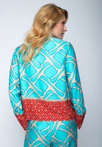 Jedwabna marynarka z turkusowo-beżowym abstrakcyjnym wzorem, czerwonymi akcentami w desenie oraz luźnym krojem z długimi rękawami.