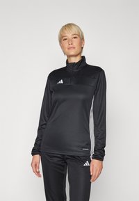 Svart atletisk quarter-zip topp i lett materiale med lange ermer. Har hvite Adidas tre striper og logo på brystet.