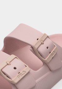 Κοντινό πλάνο ροζ σανδαλιών με ρυθμιζόμενους ιμάντες με αγκράφες που φέρουν τη μάρκα FILA.