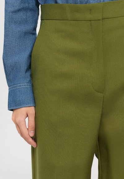 Pantaloni su misura color verde oliva con una texture liscia, una vita alta e dettagli sulle tasche anteriori, abbinati a una camicia in denim blu.
