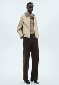 Veste cropped beige avec un col noir, associée à un col roulé taupe et un pantalon à carreaux marron. Des bottines noires à la cheville complètent la tenue.