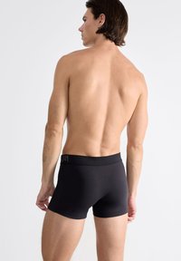 Boxer-briefs en coton noir avec une ceinture élastique douce et un détail de logo. Texture lisse, design ajusté et longueur mi-cuisse.