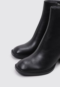 Botas de cuero negro hasta el tobillo con puntera redondeada y textura suave, que presentan líneas elegantes y sutiles detalles de costura. Diseño con tacón.