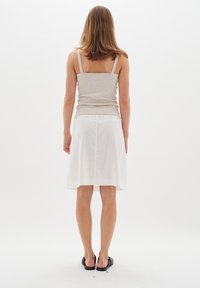 Graues Tanktop, weißer Leinenrock mit elastischem Bund. Flache schwarze Sandalen. Einfarbig, keine Muster, geradliniges Design.