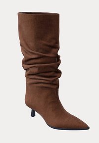 Bottine en daim marron avec une tige souple, un bout pointu et un petit talon carré. Présente une texture lisse et un design élégant.