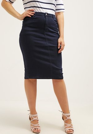 Donna che indossa una gonna a matita blu navy al ginocchio, una maglietta a maniche corte a righe bianche e blu navy, e tacchi alti beige con cinturini.