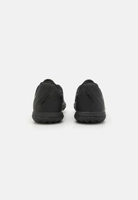 Chaussures de sport noires avec une semelle en caoutchouc texturé, un dessus en synthétique lisse et un design minimaliste. Présente une marque sur le talon.