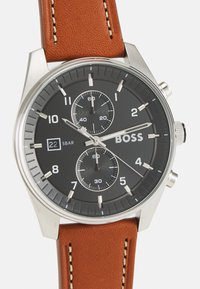 Orologio in acciaio inossidabile argento con quadrante nero, sub-quadranti cronografici, visualizzazione della data e cinturino in pelle marrone con cuciture crema.