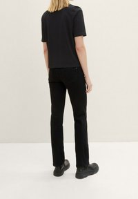 Camiseta negra de manga corta con corte recto, combinada con jeans negros de corte recto. El calzado presenta suelas gruesas en negro. Fondo neutro.