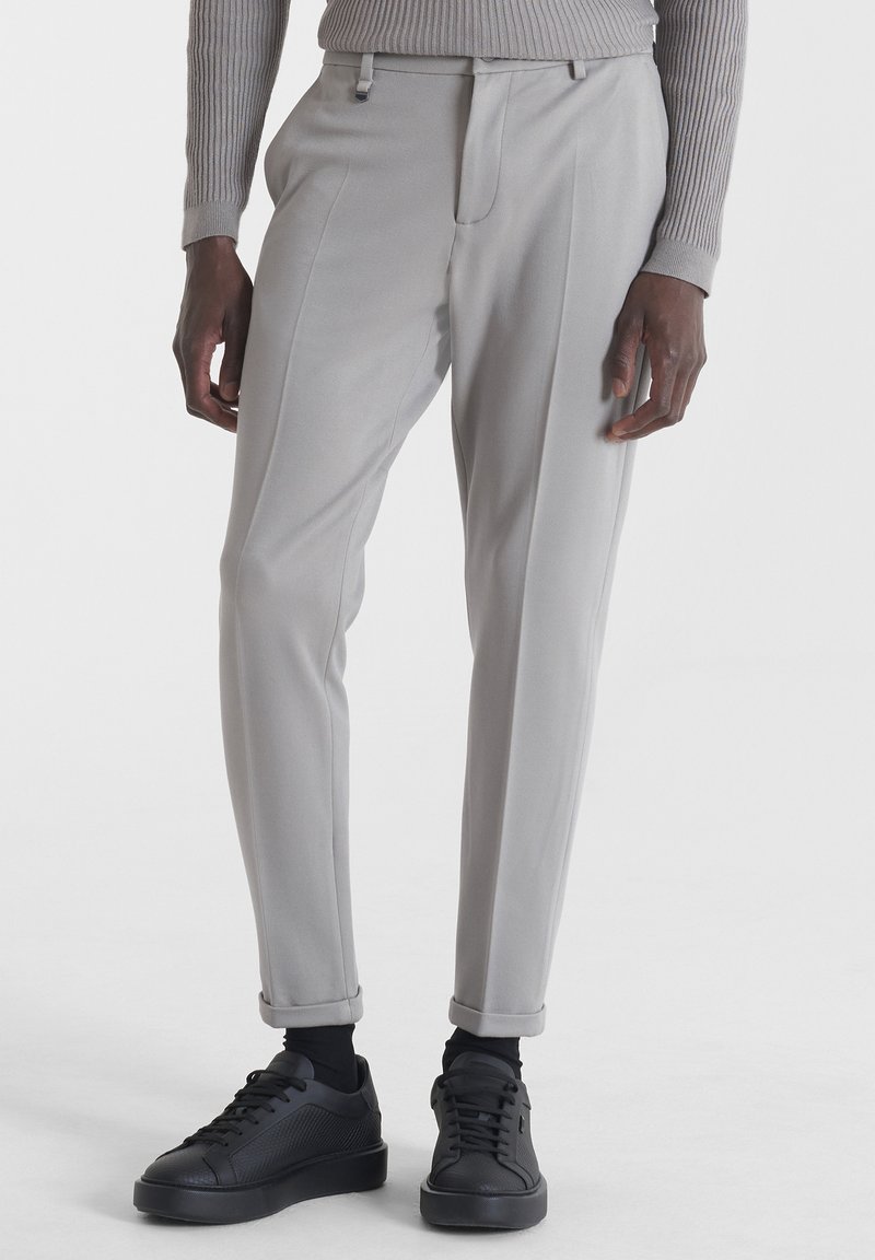 Pantaloni grigi chiari su misura con una vestibilità affusolata, caratterizzati da una piega frontale, passanti per cintura e orli arrotolati, abbinati a sneaker nere.