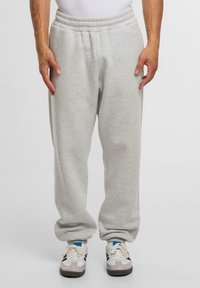 Graue Sweatpants aus weichem Stoff mit einem elastischen Bund, Seitentaschen und einer lockeren Passform, kombiniert mit weißen und grauen Sportschuhen.