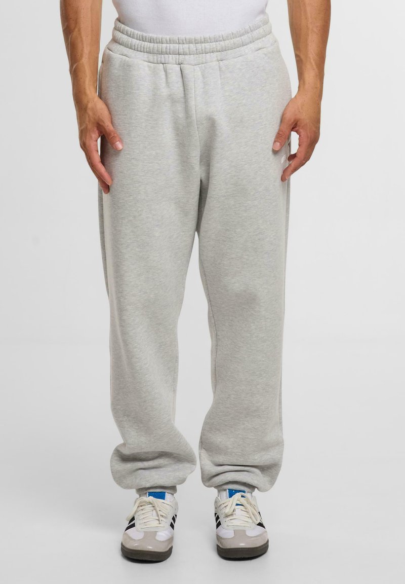 Graue Sweatpants aus weichem Stoff mit einem elastischen Bund, Seitentaschen und einer lockeren Passform, kombiniert mit weißen und grauen Sportschuhen.