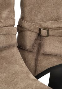 Primer plano de botines de ante topo con correas envolventes y una pequeña hebilla de bronce en tacones cuadrados negros.