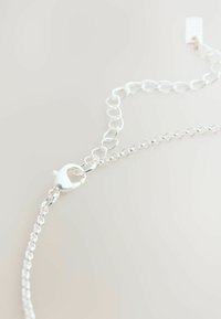 Bracelet en chaîne argentée avec des maillons ovales, un fermoir en forme de cœur et une fine chaîne d'extension pour un ajustement en longueur. Fini poli.