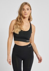 Svart sport-bh med rundad halsringning och breda axelband, med en texturerad design och logodetalj. Kombinerad med högmidjade svarta leggings.