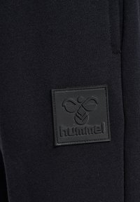 Zwart gebreid stof met een rechthoekig zwart rubberen label waarin het "hummel" logo in het midden is gebosst.