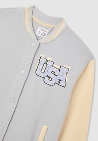 Szara kurtka bombowiec z beżowymi rękawami, z niebieską i białą haftowaną literą "USA". Zapięcie na napy i detal ściągacza przy kołnierzu. Miękka tekstura materiału.