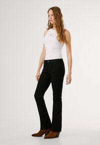 Jeans flare in denim nero abbinati a un top senza maniche bianco con un piccolo logo, completati da tacchi a zeppa in suede marrone.