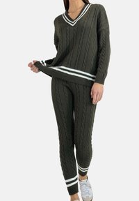 Ciemnozielony sweter z dzianiny warkoczowej i pasujące spodnie, ozdobione białymi paskami na mankietach i dole. Miękka tekstura i luźny krój.