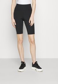 Zwarte fietsshorts met een hoge tailleband, voorzien van witte zijstrepen en een soepele, rekbare stof. Gecombineerd met zwarte sportschoenen.
