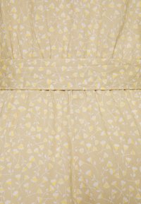 Gul blommönstrad tyg med vita och ljusgula blommor mot en beige bakgrund. Anmärkningsvärda veck och en samlad midjedesign.