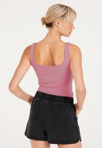 Fitted roze geribbelde tanktop gecombineerd met zwarte korte broeken met een elastische tailleband en zijzakken. De achterkant toont een vierkante halslijn.