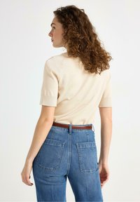 Maglione beige a maniche corte con scollo rotondo, abbinato a jeans di denim blu a vita alta con due tasche posteriori e una cintura marrone.