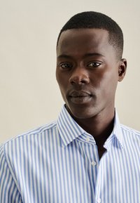 Camicia a righe blu e bianche con colletto button-down, caratterizzata da una texture liscia e un fit classico, indossata da un modello.