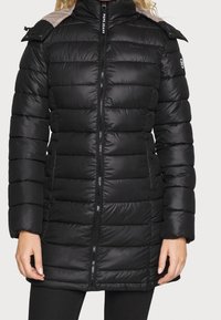Černý péřový kabát s horizontálním prošíváním, vysokým límcem, předním zipem a šedými ramenními akcenty. Obsahuje logo na rukávu.