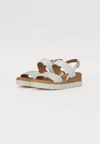 White wedge sandals with cross-strap design, woven front, cork midsole, and rubber outsole, showcasing a smooth texture and minimal accents.