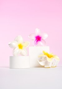 Tre blomformade hårklämmor på vita socklar. Färger: vit med gul mitt, rosa med rosa mitt och gul med vita detaljer.