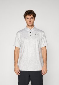 Hvid polo-shirt med korte ærmer og et helblomstret mønster, tre-knaps placket og et sort Nike-logo på venstre bryst.