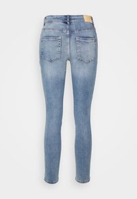 Vaqueros ajustados azul claro con dos bolsillos traseros y una etiqueta de cuero marrón claro en la cinturilla, mostrados desde la parte trasera.