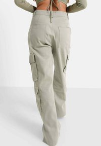 Pantalons cargo gris clair à taille haute, dotés de multiples poches à rabat et d'une coupe décontractée, fabriqués en tissu texturé. Fermeture éclair au dos.