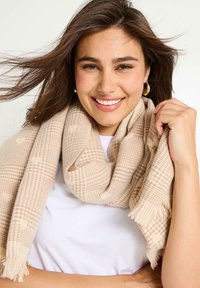 Bufanda a rayas beige con bordes desflecados, hecha de una tela suave. Lleva puesta de forma suelta alrededor del cuello, añadiendo textura y calidez.