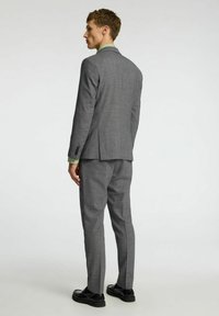 Grijze op maat gemaakte jas met een notch lapel, slim-fit ontwerp, gestructureerde stof en enkele split. Vergezeld van een lichtgroen shirt en zwarte schoenen.
