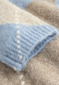 Zbliżenie na miękką dzianinę, pokazujące przytulną jasnoniebieską i beżową wełnę z prążkowaną fakturą oraz drobnymi białymi szwami.