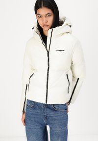 White puffer jacket featuring a high collar, zip closure, black accents, and logo. Paired with blue denim jeans. Smooth, padded texture.