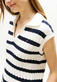 Sweter polo o charakterze dzianinowym, z granatowo-białymi poziomymi paskami, krótkimi rękawami i prążkowaną fakturą. Małe logo marki na piersi.