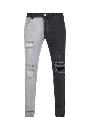 Jean skinny bicolore avec une jambe gauche gris clair et une jambe droite gris foncé, déchiré avec des rips, et un accent de logo sur le bas de la jambe.