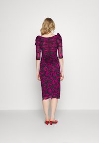 Tajt, midiklänning i klar rosa med svart blommönster, med puffy ärmar och rynkad textur. Enkel fåll. Röda klacksandaler.