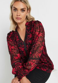 Schwarze Chiffonbluse mit rotem Blumenmuster, gerafften langen Ärmeln und einem Knopf-V-Ausschnitt, der mit schwarzen und weißen Punktdetails akzentuiert ist.