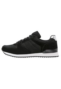 Chaussure de sport noire avec tige en mesh et en daim, bout rond, design à lacets, accents argentés sur le talon et semelle extérieure blanche avec un motif de traction.