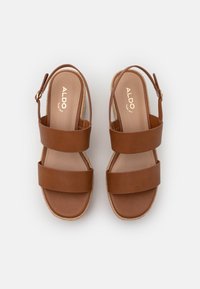 Brune skinnsandaler med to brede stropper og slingback-design, med en vevd jute såle og en glatt, matt overflate.