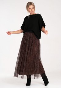 Czarny oversized sweter połączony z brązową spódnicą maxi z tiulu w panterkę, z marszczoną talią i zwiewnymi warstwami. Czarne botki do kostek.