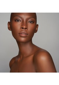 Portrett av en person med mørk hud, jevn tekstur og veldefinerte ansiktstrekk. Kort hår, nøytral sminke som fremhever naturlig skjønnhet og konturer.