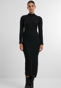Abito midi nero a maniche lunghe con collo alto, silhouette aderente e spacchi laterali. Realizzato in un tessuto morbido e elastico.